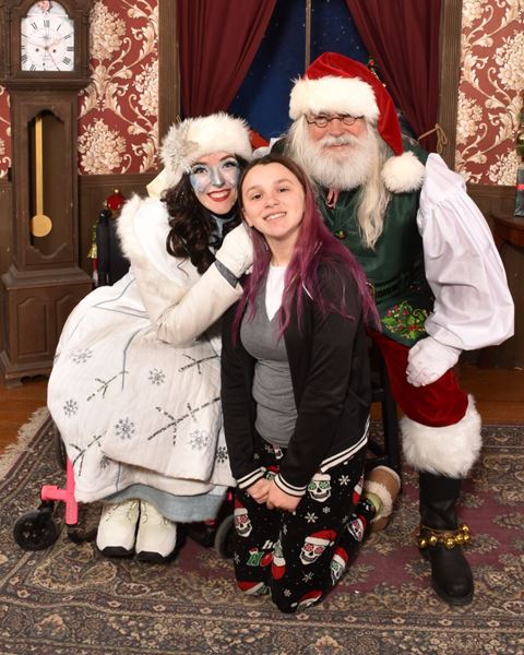 A teenager kneeling between Santa and a snow queen character