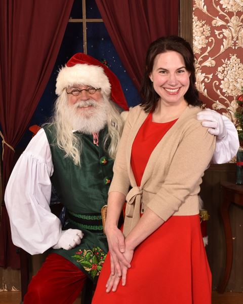 A smiling woman in a red dress seated beside Santa